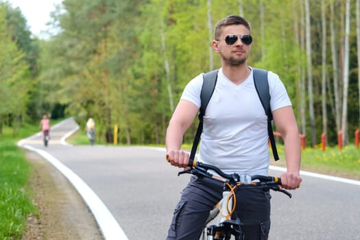 A cyclist with a backpack and glasses rides a bicycle on a forest road enjoying nature.