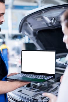 Licensed repairman in garage using mockup laptop to follow checklist while doing maintenance on car. Meticulous expert in auto repair shop does checkup on vehicle helped by isolated screen device