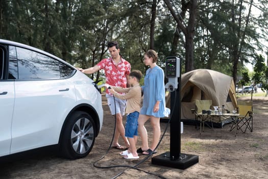 Outdoor adventure and family vacation camping in nature travel by eco friendly car for sustainable future. Lovely family recharge EV car with EV charging station in campsite. Perpetual