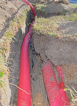 Cables in the trench. High voltage cables in protective red cover in the trench. Concept of electrical installations, construction works, building renovations and building refurbishments.