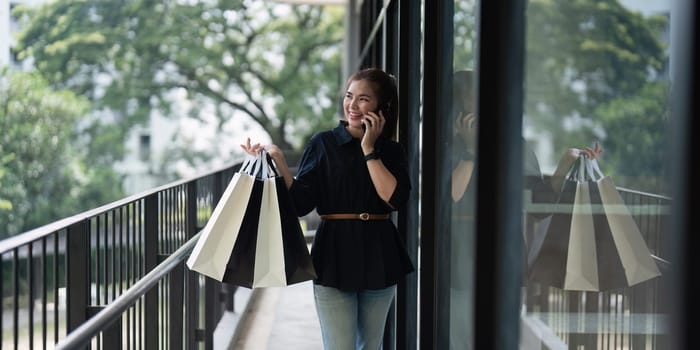 Young woman standing at road holding shopping bags and using mobile phone. Purchases, black friday, discount.