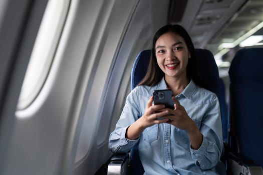 Asian people female person onboard, airplane window, using mobile and looking at camera while on the plane.