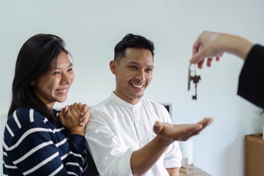 Happy real state agent giving new house key to a young couple. Real estate concept.