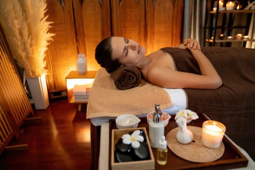 Caucasian woman customer enjoying relaxing anti-stress spa massage and pampering with beauty skin recreation leisure in warm candle lighting ambient salon spa at luxury resort or hotel. Quiescent