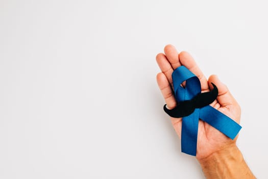 In November, show your support for men's health and Prostate cancer awareness. Hands hold a light blue ribbon with a mustache on a blue background a symbol of unity.