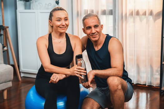 Athletic and sporty senior couple portrait in sportswear sitting on sofa with fitness water bottle as home exercise concept. Healthy fit body lifestyle after retirement. Clout