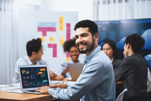 Portrait of happy and smiling businessman with group of coworkers on meeting with screen display business dashboard in background. Confident office worker at team meeting. Concord