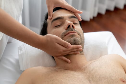 Caucasian man enjoying relaxing anti-stress head massage and pampering facial beauty skin recreation leisure in dayspa modern light ambient at luxury resort or hotel spa salon. Quiescent