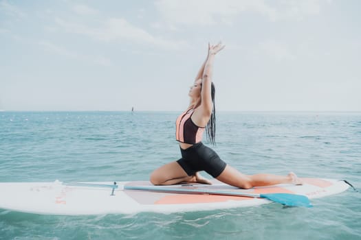 Woman sup yoga. Happy young sporty woman practising yoga pilates on paddle sup surfboard. Female stretching doing workout on sea water. Modern individual female outdoor summer sport activity