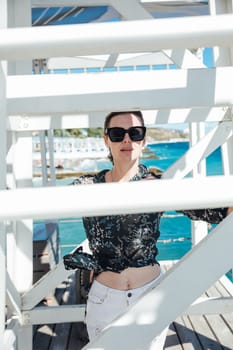 A woman wearing sunglasses near a rescue tower by the sea