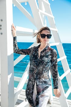 A woman wearing sunglasses near a rescue tower by the sea