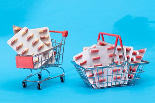 Buying Medicines. Drug Addiction Concept: Pills and Capsules in Shopping Cart on Blue Background. Global Pharmaceutical Industry and Big Pharma. Ordering Pharmaceutical Products