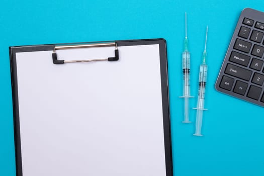 Vaccination, Immunology or Revaccination Concept - Two Medical Syringe Lying on Blue Table in Doctor's Office in a Hospital or Clinic. Black Clipboard with Sheet of Paper - Mock Up with Copy Space