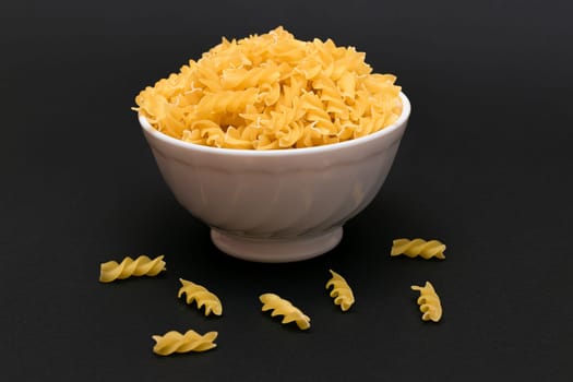 Uncooked Fusilli Pasta in White Bowl on Black Table. Raw and Dry Macaroni. Unhealthy and Fat Food. Italian Culture