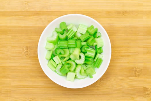 Fresh Chopped Celery Slices in White Bowl on Bamboo Cutting Board - Top View. Vegan and Vegetarian Culture. Raw Food. Healthy Diet with Negative Calorie Content