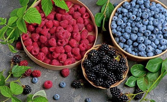 A variety of summer berries - raspberries, strawberries blueberries, - in cups on a wooden table