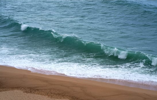 Top view over the sea beach. Beautiful sea waves. Sandy beach and stunning sea. Summer sunset seascape. Water texture. Human footprints on wet sand.