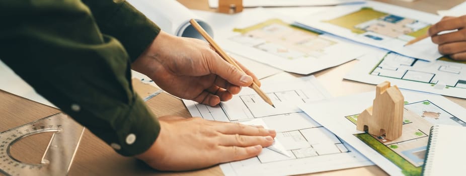 Professional engineer team discussion about house design on meeting table with architectural equipment and blueprint scatter around at modern office. Focus on hand. Closeup. Delineation.