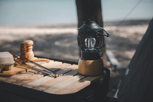 An antique kerosene lantern and a bright LED camping lamp on a wooden table at the beach. Perfect for summer camping and outdoor travel. Old meets new in the great outdoors.