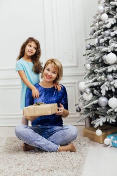 Mom with little girl at christmas tree with gifts and toys