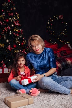 Mom with little girl at christmas tree with gifts and toys