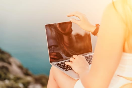 Freelance women sea working on the computer. Good looking middle aged woman typing on a laptop keyboard outdoors with a beautiful sea view. The concept of remote work