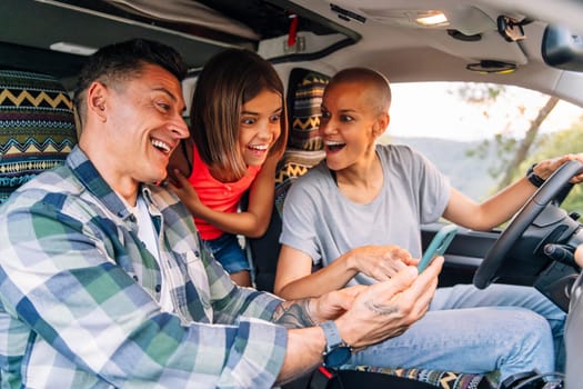 happy family planning on the mobile phone the route through the countryside in their camper van, concept of adventure travel with children and active tourism in nature