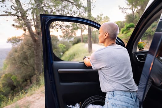 rear view of a woman leaning on the door of her van admiring the landscape in the countryside, concept of adventure travel and active tourism in nature