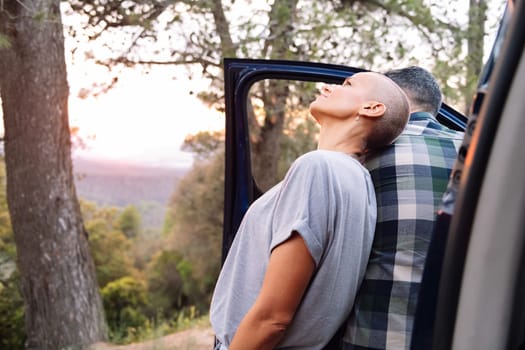 woman and man leaning on the door of their van admiring the landscape in the countryside, concept of couple adventure travel and active tourism in nature