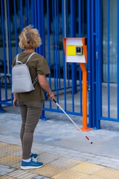 An elderly blind woman goes to a button to call help for people with disabilities. Vertical photo