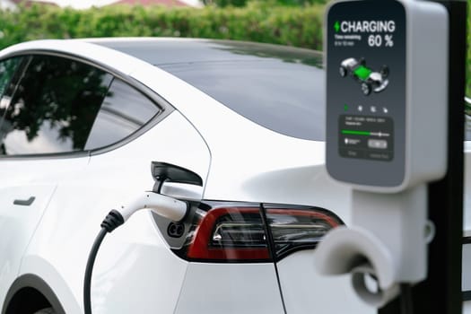 Closeup EV charger plug handle attached to electric vehicle port, recharging battery from charging station. Modern designed EV car and clean energy sustainability for better future concept. Synchronos