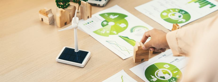 Environmental documents and a windmill model representing the use of clean energy are scattered on the table during a green business discussion about investing in clean energy. Closeup. Delineation.