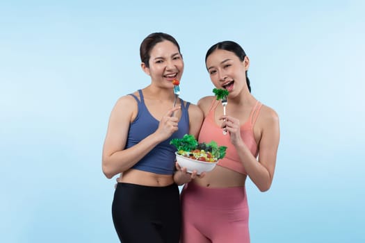 Two young sporty Asian women in sportswear holding salad bowl fill with fruit and vegetable. Natural youthful and fit body lifestyle people with balance nutrition on isolated background. Vigorous