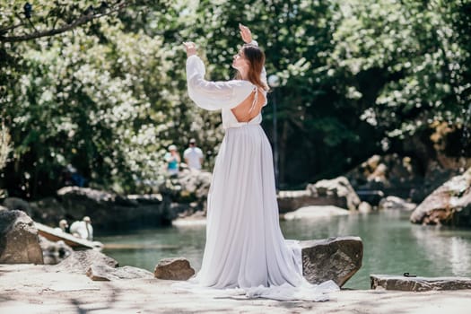 a beautiful woman in a long white dress looks into the distance at a beautiful lake with swans