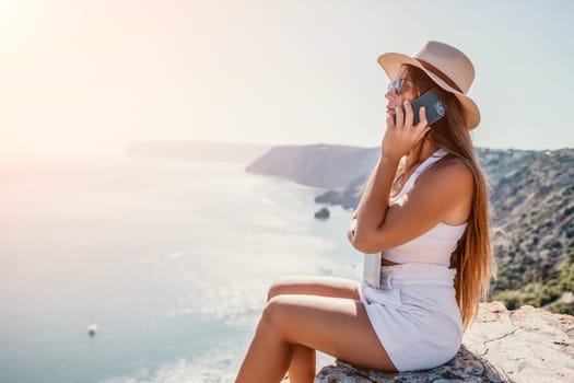 Successful business woman in yellow hat working on laptop by the sea. Pretty lady typing on computer at summer day outdoors. Freelance, travel and holidays concept.