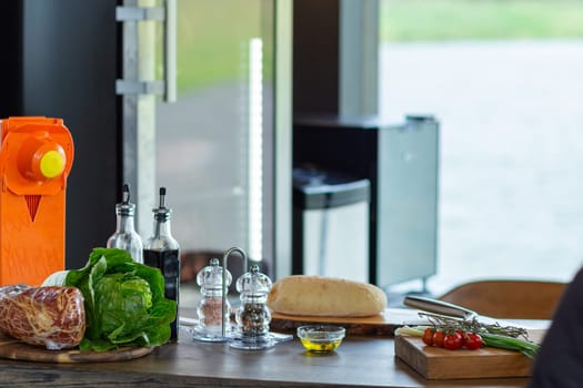 Fresh ingredients for cooking snacks on table. The interior of a modern kitchen with a transparent wall, behind which the surface of the lake is visible.