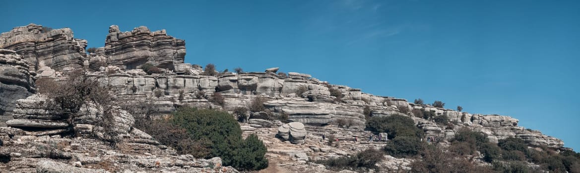 Unrecognizable tourists hike in a line through the layered rocks of Torcal de Antequera, with space for text.
