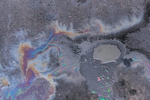 Rainbow-colored oil floating on water after rain on asphalt. Gasoline stains. Colored texture, natural background.