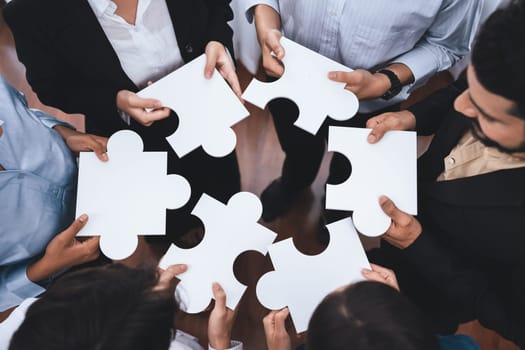 Diverse corporate officer workers collaborate in office, connecting puzzle pieces to represent partnership and teamwork. Unity and synergy in business concept by merging jigsaw puzzle. Concord