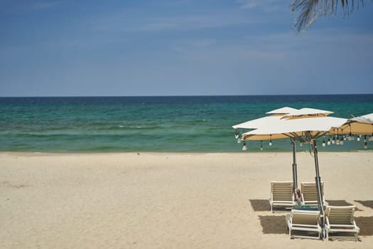 Straw sunshades and sunbeds on the empty pebble beach with sea in the background. Deserted beach with rattan sun loungers and umbrellas