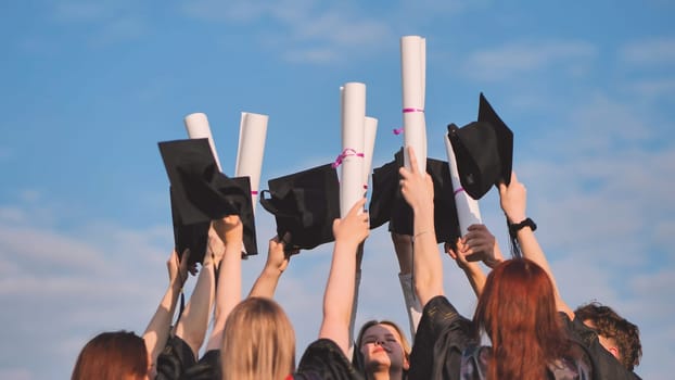 College graduates raise their hands with caps and diplomas to the sky