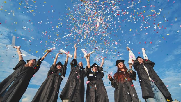 Happy graduates throw colorful confetti against a blue sky