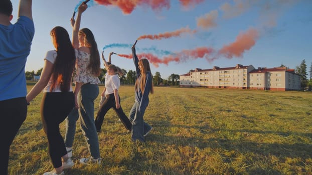 A group of friends spraying multi-colored smoke at sunset