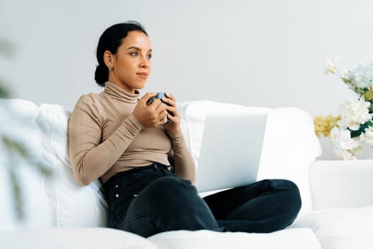 Happy woman drinking coffee on a sofa at home for crucial rest and relaxation. Portrait of young African American woman holding a cup.