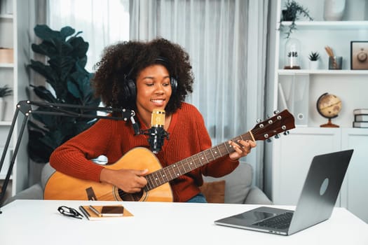 Host channel in musician of young African American playing guitar along with singing, broadcasting on laptop in studio. Decoration of equipment of headsets and recording microphone. Tastemaker.