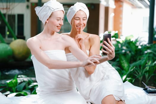 Couple of young beautiful women with beautiful skin in white towel taking a photo together at outdoor surrounded by peaceful natural environment. Beauty and healthy spa concept. Tranquility.