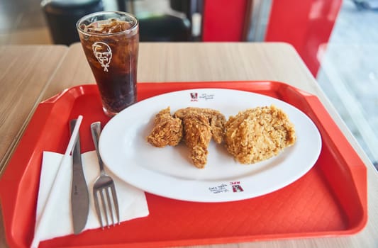 Danang, Vietnam - 06.27.2023: Lunch at a fast food cafe. KFC wings on a plate of Coca-Cola. High quality photo