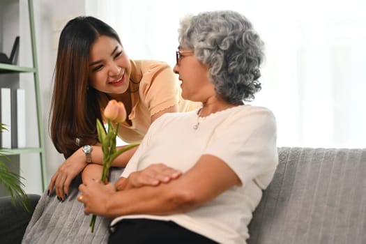 Shot of happy senior mother receiving beautiful spring tulips from her daughter.