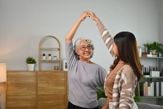 Overjoyed senior mother and adult daughter dancing in cozy living room. Family and leisure active concept.
