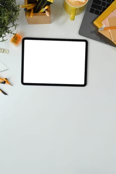 Flat lay, top view digital tablet with white empty screen, coffee cup and laptop on white table.